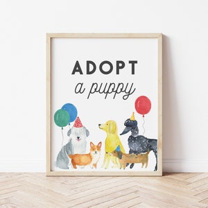 May include: A white framed print with the text "ADOPT a puppy" in black. The print features a watercolor illustration of five dogs wearing party hats and surrounded by balloons.