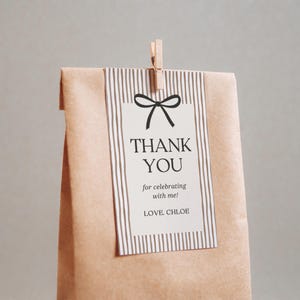 Pode incluir: Uma sacola de presente de papel marrom com uma etiqueta listrada que diz "THANK YOU" e "for celebrating with me!". A etiqueta &eacute; presa por um prendedor de roupa de madeira. A sacola &eacute; dobrada na parte superior.