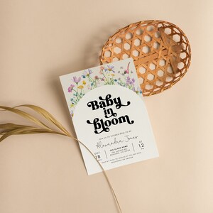 May include: A white baby shower invitation with a floral border and the text "Baby in Bloom" in a retro font. The invitation includes the date, time, and location of the event.