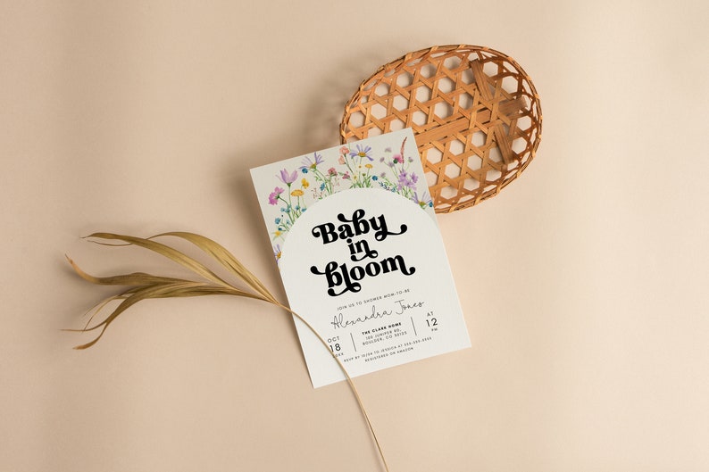 May include: A white baby shower invitation with a floral border and the text "Baby in Bloom" in a retro font. The invitation includes the date, time, and location of the event.