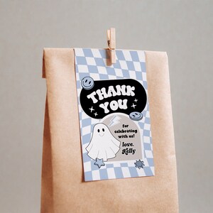 May include: A brown paper gift bag with a light blue and white checkered tag. The tag says "THANK YOU" in a black oval with smiley faces and stars. A ghost illustration and the text "for celebrating with us! love, Kelly" are also on the tag.