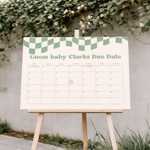 May include: A rectangular sign on a wooden easel featuring a cream background with a sage green checkered border at the top. The text reads Guess baby Clarks Due Date above a calendar grid with the months of March and April and the words Due Date.
