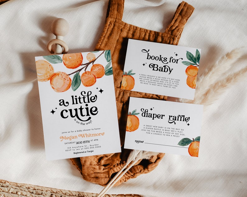 May include: A baby shower invitation with orange and green illustrations of oranges and leaves. The invitation reads "a little cutie is on the way" and includes the name Megan Whitmore and the date Saturday August 15th at 4pm. There are also two cards for a book and diaper raffle.