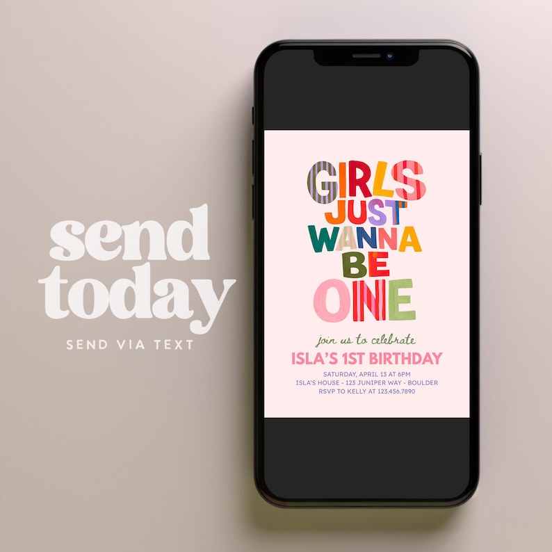 May include: A smartphone displaying a digital birthday invitation with the colorful text GIRLS JUST WANNA BE ONE. The invitation includes details for Isla's 1st birthday on Saturday, April 13 at 6pm at Isla's house, 123 Juniper Way, Boulder, RSVP to Kelly.