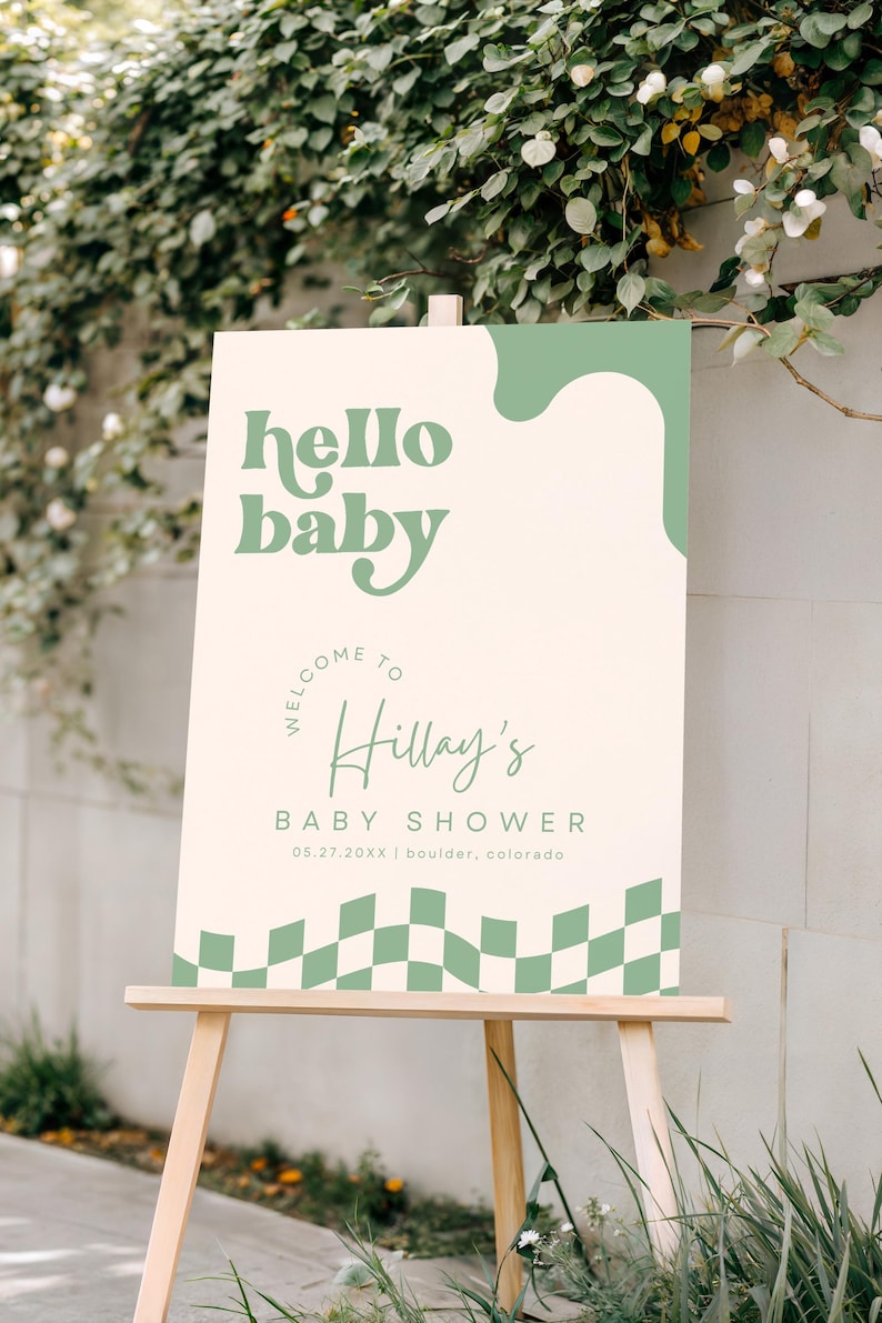 May include: A rectangular welcome sign for a baby shower featuring a cream background with sage green accents. The text reads hello baby, welcome to Hillay's baby shower, 05.27.20XX, and boulder, colorado. The bottom edge has a sage green checkered pattern.