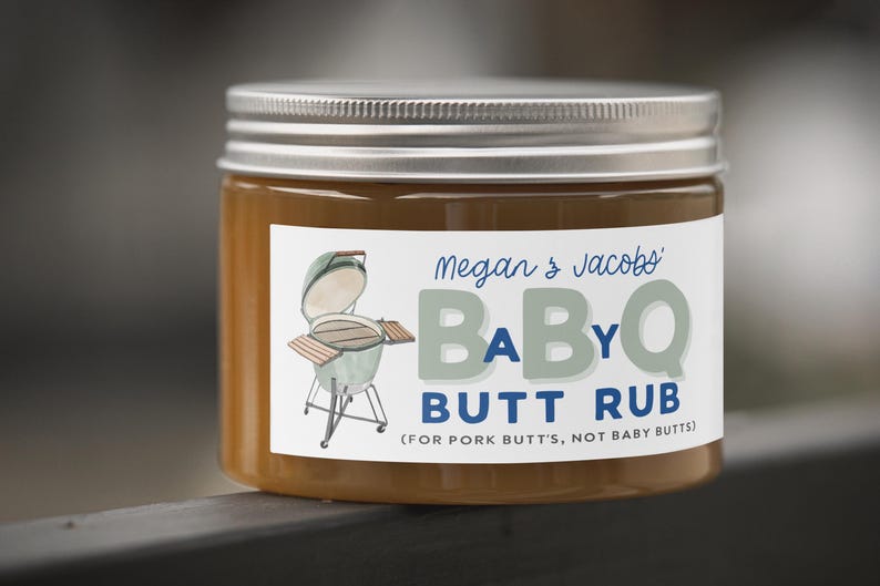 May include: A jar of BBQ butt rub with a silver lid and a white label. The label features the text "Megan & Jacobs BABYQ BUTT RUB" and an illustration of a grill. The jar is filled with a brown substance.