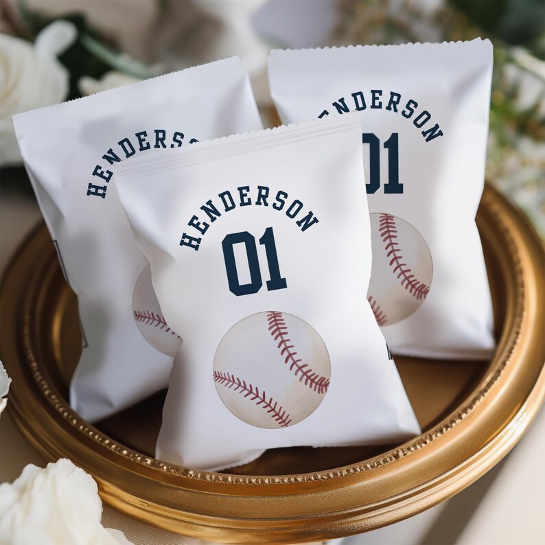 K&ouml;nnte beinhalten: Drei wei&szlig;e Papiert&uuml;ten mit Baseball-Motiv. Jede T&uuml;te hat ein Baseball-Motiv, den Namen "Henderson" und die Nummer "01" aufgedruckt.