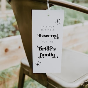 K&ouml;nnte beinhalten: Ein wei&szlig;es Schild mit schwarzem Text, der "This row is kindly reserved for the bride's family" lautet. Das Schild h&auml;ngt an einem Metallstuhl mit einer wei&szlig;en Schnur.