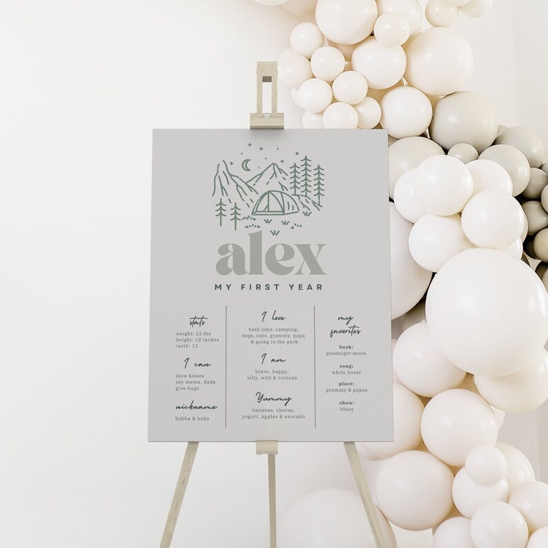 May include: A light gray poster with a green illustration of a mountain range and a tent. The poster says "alex" in gray text and "My First Year" in smaller gray text. The poster is divided into three columns with the headings "Stats", "I Love", and "My Favorites". The poster lists information about the child's first year, including weight, height, and favorite foods.
