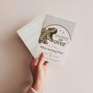 Puede incluir: Una tarjeta de invitaci&oacute;n de cumplea&ntilde;os rectangular con un T-Rex verde con gafas de sol naranjas, hojas de palma y el texto "stomp on over", "Miles turning Five!", "saturday sept. 14" y "2-4 pm". La tarjeta tiene un fondo blanco con finas rayas grises.