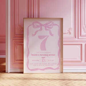 May include: Pink invitation card with a white background and a pink ribbon bow. The text on the card reads "Join us to celebrate Annie's turning seven! Apr. 13, Saturday, 2-4 pm, Clark House, 123 Juniper Way, Boulder, RSVP to Kelly at 123.456.7890."