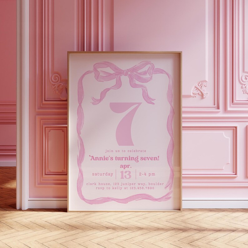 May include: Pink invitation card with a white background and a pink ribbon bow. The text on the card reads "Join us to celebrate Annie's turning seven! Apr. 13, Saturday, 2-4 pm, Clark House, 123 Juniper Way, Boulder, RSVP to Kelly at 123.456.7890."