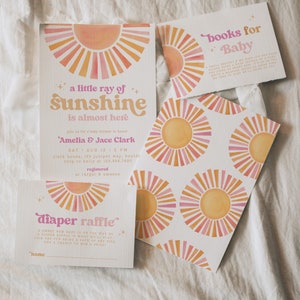 Peut inclure: Une invitation de f&ecirc;te pr&eacute;natale avec un motif de soleil aquarelle. L'invitation indique "un petit rayon de soleil arrive bient&ocirc;t" et comprend les noms Amelia & Jace Clark, la date et l'heure de la f&ecirc;te, ainsi que l'adresse. L'invitation comprend &eacute;galement une carte de tombola pour les couches avec un motif de soleil aquarelle.