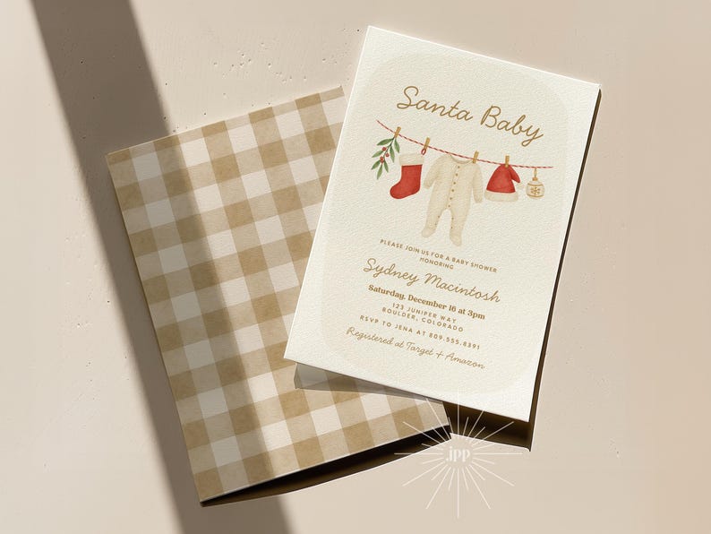 May include: A baby shower invitation with the text "Santa Baby" and a watercolor illustration of baby clothes hanging on a clothesline. The invitation is cream-colored with a gingham envelope.