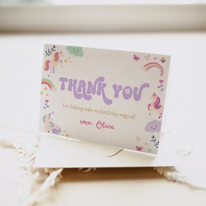 Puede incluir: Una tarjeta de agradecimiento con un dise&ntilde;o de unicornio, arco&iacute;ris y nubes en morado y rosa. El texto dice "THANK YOU for helping make my birthday magical! xoxo. Olivia."