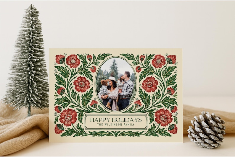 May include: Christmas card featuring a family photograph within an oval frame, framed by a floral pattern of red flowers and green foliage. The text reads "HAPPY HOLIDAYS" and the family name. A small Christmas tree and pine cone are in the background.