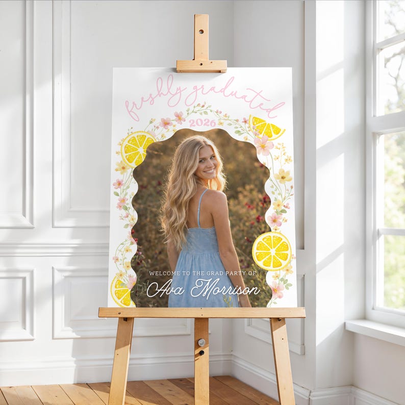 K&ouml;nnte beinhalten: Willkommensschild f&uuml;r eine Abschlussfeier auf einer Holzstaffelei. Das Schild zeigt ein Foto einer Frau in einem blauen Kleid, umgeben von einem floralen und Zitronen-Design. Der Text enth&auml;lt "freshly graduated" und "Welcome to the Grad Party of Ava Morrison."