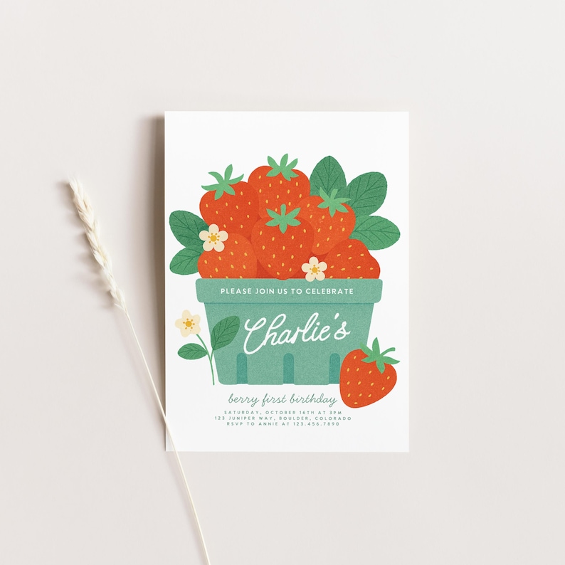 May include: A white invitation card with a berry theme. It features a green basket overflowing with red strawberries, green leaves, and white flowers. The text "PLEASE JOIN US TO CELEBRATE" is above the name "Charlie's". The text "berry first birthday" is below.