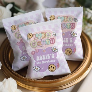 May include: Purple and white party favor bags with a checkered pattern. The bags have a colorful "Let's Party" design with a smiley face, flowers, and stars. The text "Abbie's 5th Birthday" is printed on the bag.