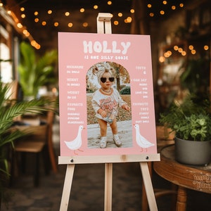 K&ouml;nnte beinhalten: Ein rosa-wei&szlig;es Schild mit dem Namen "HOLLY" in einer verspielten Schriftart. Das Schild listet Informationen &uuml;ber Holly auf, darunter ihren Spitznamen, ihre Gr&ouml;&szlig;e, ihr Gewicht, ihre Lieblingsessen und ihre Lieblingsspielzeuge. Ein Foto von Holly ist auf dem Schild enthalten.
