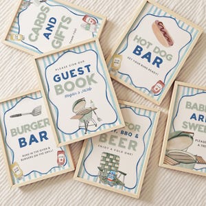 May include: A collection of framed signs with watercolor illustrations and text for a barbecue. Signs include "Cards and Gifts", "Guest Book", "Burger Bar", "Hot Dog Bar", "For BBQ & Beer", and "Babies are Sweet". Each sign has a light wood frame.