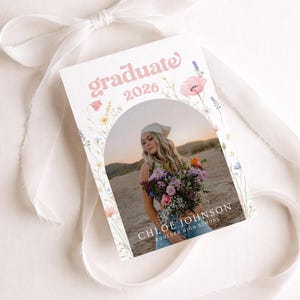 Puede incluir: Una tarjeta de anuncio de graduaci&oacute;n con la palabra "graduate" en escritura rosa y el a&ntilde;o "2026". La tarjeta presenta una foto de una persona sosteniendo flores, con el nombre "Chloe Johnson" y "Boulder High School" impresos debajo. Borde floral.