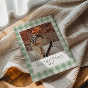 May include: A photo album with a green and white gingham border. The album features a photo of a child on a skateboard. The album has the name "Karter Dean" and the year "20XX" printed on the front.
