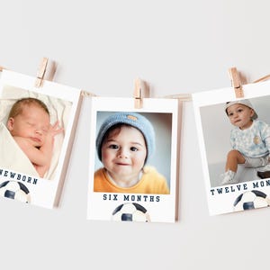 May include: Three white photo frames with black borders, each showing a baby at different ages. The frames are hung on a string with clothespins. The frames are labeled "Newborn", "Six Months", and "Twelve Months". Each frame has a soccer ball graphic at the bottom.