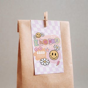 May include: A pink and purple thank you card with a checkered background. The card features a smiley face, peace sign, flowers, and the text "thanks good times".