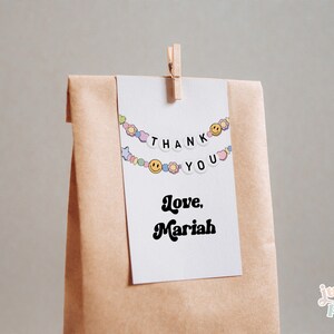 May include: A white card with a colorful beaded garland that says "Thank You" and "Love, Mariah" in black text. The card is attached to a brown paper bag.