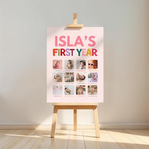 May include: A light pink poster titled ISLA'S FIRST YEAR in bold letters, featuring twelve square photographs arranged in a grid. Each photo is labeled with a month from 1 month to 12 months, documenting a baby's growth milestones.