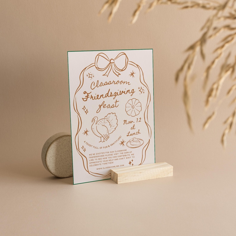 May include: A brown and white card with a green border. The card has a festive illustration of a turkey, a pie, and a flower. The text on the card reads "Classroom Friendsgiving Feast Nov. 12 at Lunch".