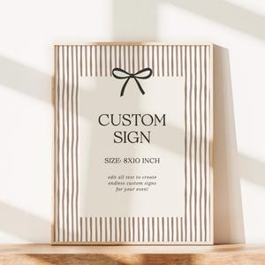 Pode incluir: Uma placa personalizada emoldurada com fundo bege e listras verticais marrons. A placa apresenta o texto "CUSTOM SIGN" e "TAMANHO: 20x25 cm" com um la&ccedil;o preto. A moldura &eacute; de cor de madeira clara.