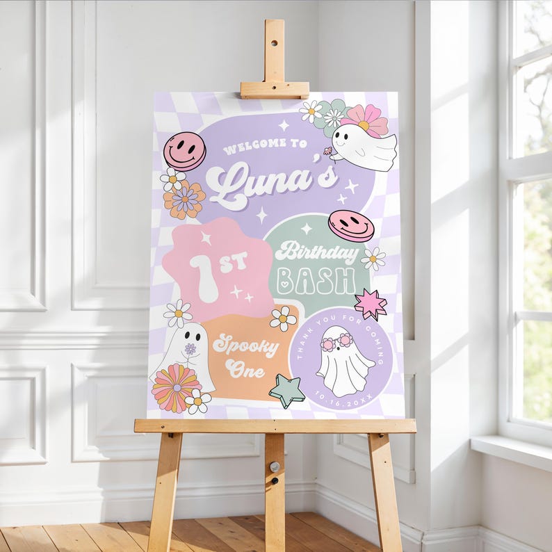 May include: A decorative sign on a wooden easel. The sign features a pastel color scheme with the words "Welcome to Luna's 1st Birthday Bash" and other text. The design includes smiley faces, ghosts, flowers, and stars.