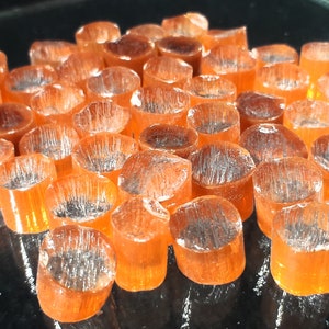 May include: A close-up of a group of small, orange glass beads. The beads are arranged in a random pattern and have a slightly translucent appearance.