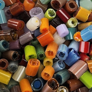 May include: A collection of colorful glass beads, featuring a variety of shapes and sizes. The beads are made of clear, opaque, and translucent glass, with a mix of colors including blue, green, orange, red, and brown.
