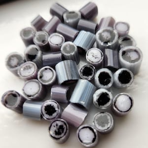 May include: A pile of small, cylindrical candy with a variety of colors, including gray, white, and black. The candy is striped and has a swirl pattern.