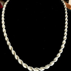 May include: A silver rope chain necklace. The chain is made of a series of interlocked links that create a rope-like appearance.