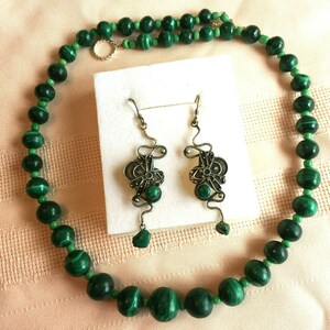 May include: A green malachite bead necklace and matching earrings with silver filigree accents. The necklace is made of round beads and the earrings are dangle style.