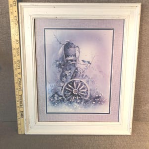 May include: A framed print featuring a vintage-style scene with a wagon wheel, flowers, and a bird. The artwork is in a white distressed wooden frame. The color palette includes shades of blue, purple, and white, creating a soft, pastoral aesthetic.