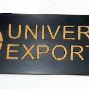 May include: Black rectangular sign with gold lettering that reads "UNIVERSAL EXPORTS". A gold globe icon is on the left side of the sign.