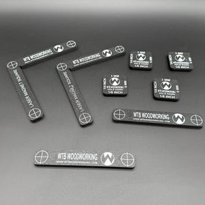 May include: A collection of black laser magnet squares and rectangular pieces with white text and graphics. The text includes "LASER MAGNET SQUARE", "WTB WOODWORKING", and measurements in inches and millimeters.