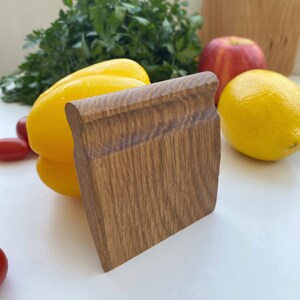 May include: A wooden kitchen tool with a smooth, brown surface. The tool is shaped like a rectangle with rounded edges. It is sitting on a white surface next to a yellow bell pepper.