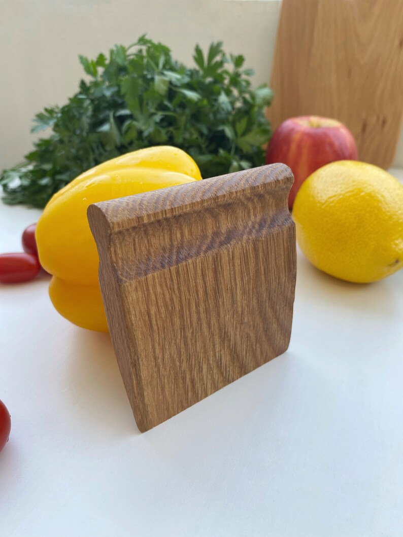 May include: A wooden kitchen tool with a smooth, brown surface. The tool is shaped like a rectangle with rounded edges. It is sitting on a white surface next to a yellow bell pepper.