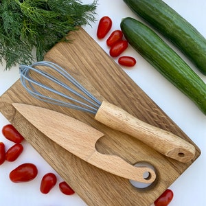 Puede incluir: Una tabla de cortar de madera con un batidor, un cuchillo de madera y un agujero en el centro. Hay tomates rojos y pepinos verdes alrededor de la tabla.