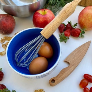 Puede incluir: Un bol azul y blanco con dos huevos marrones, un batidor y un mango de madera. Tambi&eacute;n hay manzanas, fresas y nueces en la imagen.
