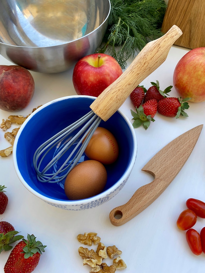 Puede incluir: Un bol azul y blanco con dos huevos marrones, un batidor y un mango de madera. Tambi&eacute;n hay manzanas, fresas y nueces en la imagen.