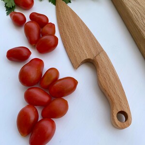 Puede incluir: Un cuchillo de madera con un mango redondeado y un agujero en el mango. El cuchillo est&aacute; sobre una superficie blanca con tomates rojos.