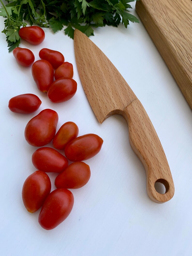 Puede incluir: Un cuchillo de madera con un mango redondeado y un agujero en el mango. El cuchillo est&aacute; sobre una superficie blanca con tomates rojos.
