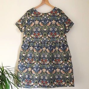 May include: A blue and green short-sleeved dress with a floral print featuring birds and flowers. The dress has a gathered skirt and a round neckline.